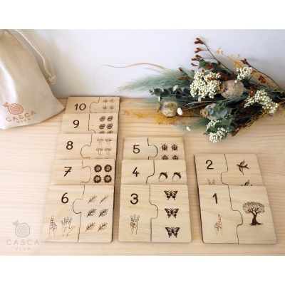 Peças de madeira numeradas com desenhos de natureza e saco de tecido CASCA VIVA numa superfície de madeira clara