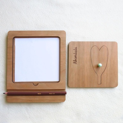 Dois quadros de madeira clara, um com folha branca e lápis, outro com drawing de coração e palavra Akzentdada.