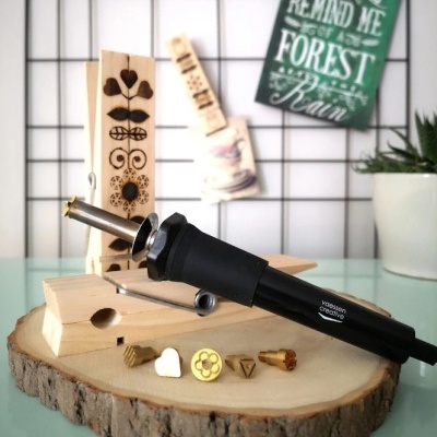 Aparelho de gravação a quente preto com acessórios metálicos numa base de madeira redonda