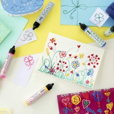 Cartões e tecido coloridos com desenhos florais e corações e tubos de tinta para tecido