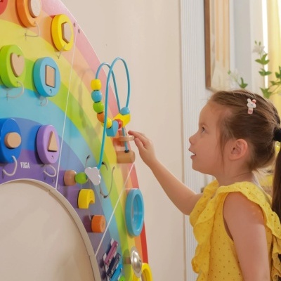 Painel de atividades colorido em madeira com formas geométricas e contas, com criança a brincar