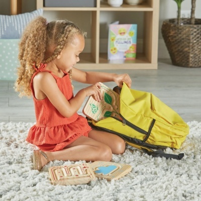 Criança com vestido vermelho e mochila amarela a brincar com brinquedos de madeira no chão