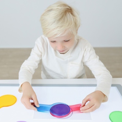 Criança brinca com peças plásticas coloridas numa mesa branca