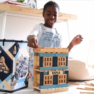 Brinquedo de blocos de madeira KAPLA formando uma casa, criança brincando ao fundo