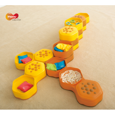 Recipientes hexagonais amarelos e castanhos com conteúdo colorido e sementes