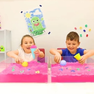 Crianças brincando com areia cinética rosa em caixas transparentes