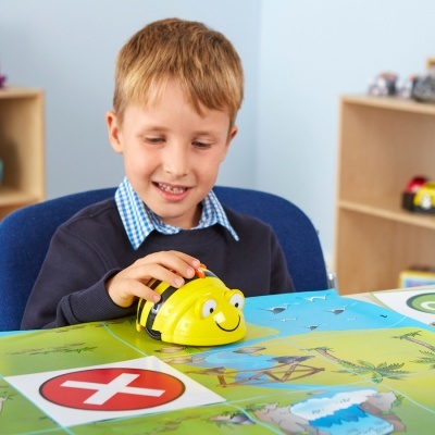 Rapaz a brincar com robô amarelo em forma de abelha numa mesa colorida