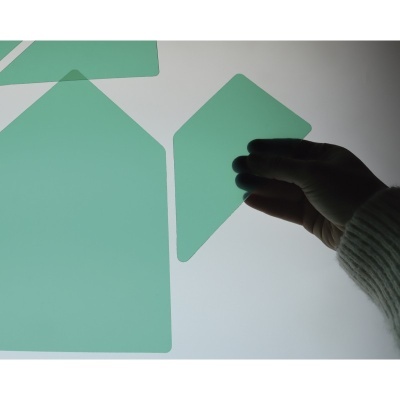 Peças verdes de plástico translúcido em fundo branco iluminado, uma segurada por mão com manga cinza