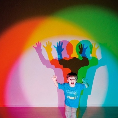 Criança com camisola azul em frente a parede com sombras coloridas