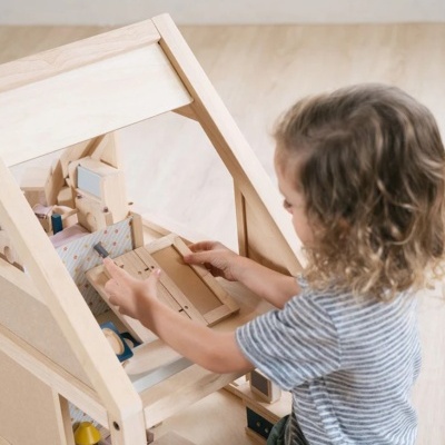 Criança a brincar com casa de bonecas em madeira clara