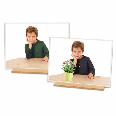 Duas fotografias de um menino com camisola verde e azul-marinho em molduras brancas sobre mesa de madeira, uma com planta verde e flores cor-de-rosa.