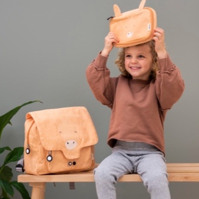 Mochilas cor de pêssego com design de animal ao lado de criança sentada