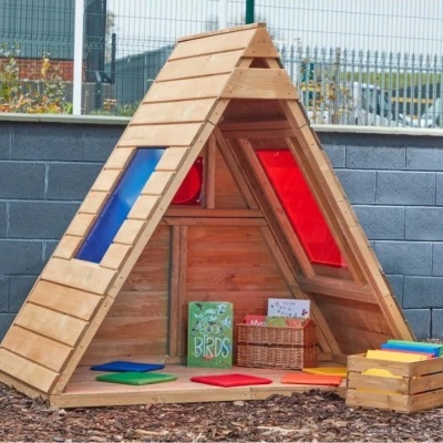 Cabana triangular de madeira com janelas coloridas e livros no chão.