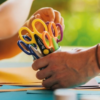 Conjunto de tesouras coloridas em recipiente metálico numa mesa com mãos próximas