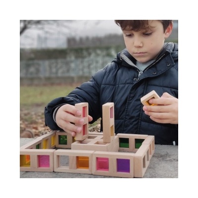 Menino a brincar com bloco de construção de madeira com janelas coloridas ao ar livre