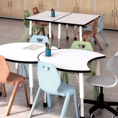 Mesa modular branca com cadeiras coloridas e cadeira giratória em espaço com chão e armários de madeira.