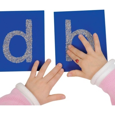 Mãos infantis segurando cartões azuis com letras prateadas 'd' e 'b'.