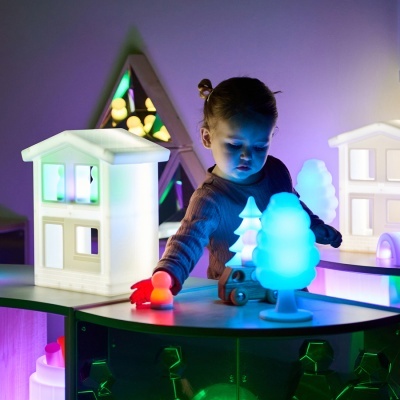 Criança a brincar com brinquedos e luzes LED coloridas em formato de casa e árvores
