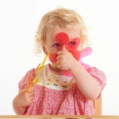 Criança com vestido rosa segurando um pincel amarelo e uma figura rosa em forma de mão
