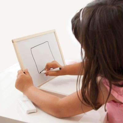Criança a desenhar num quadro branco com moldura de madeira com marcador preto.