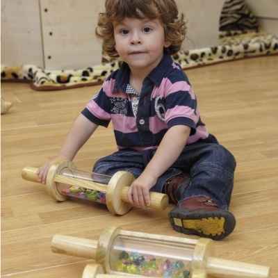 Criança sentada segurando brinquedo cilíndrico de madeira com peças coloridas dentro