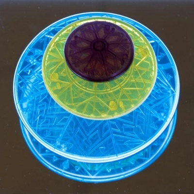 Recipientes redondos de plástico azul, amarelo e roxo empilhados com padrões geométricos.