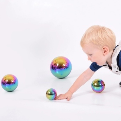 Bolas metálicas iridescentes coloridas e criança loira tocando numa delas