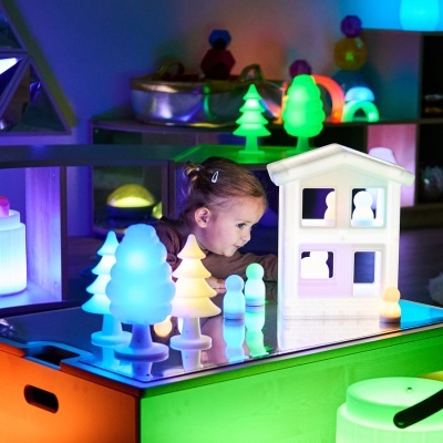 Brinquedos luminosos de silicone coloridos em forma de árvores, bonecos e casa numa mesa, criança a brincar no interior