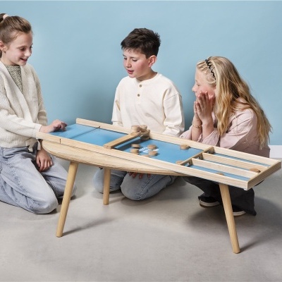 Mesa de jogos em madeira clara com tabuleiro azul e crianças a jogar