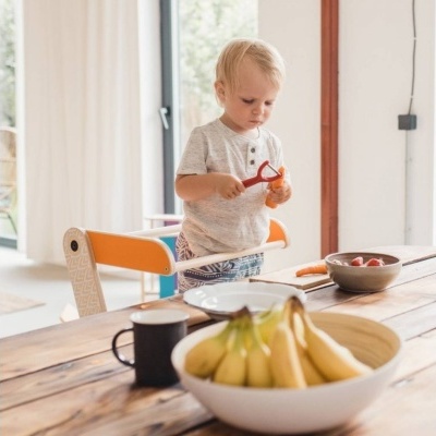 Criança loira em mesa de madeira com frutas e chávena