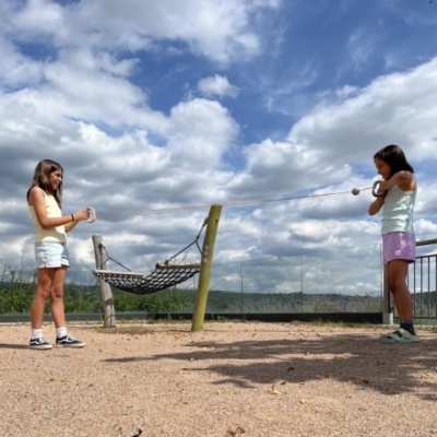 Duas raparigas a brincar ao elástico ao ar livre com céu parcialmente nublado
