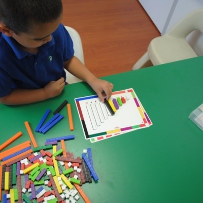 Criança a brincar com blocos de contar de várias cores numa mesa verde