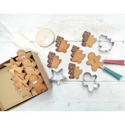 Biscoitos de gengibre decorados com formas de homem e árvore de Natal, cortadores de metal e glacê colorido numa mesa branca.