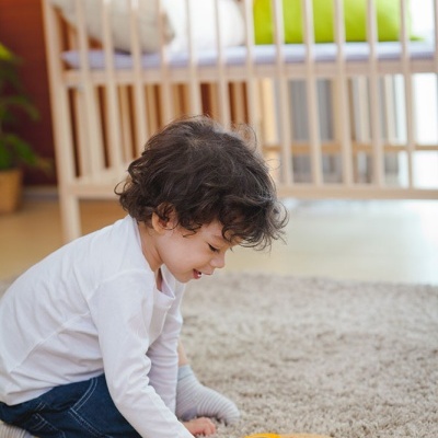 Cama bebé de madeira clara com brinquedo de madeira e criança sentada no tapete