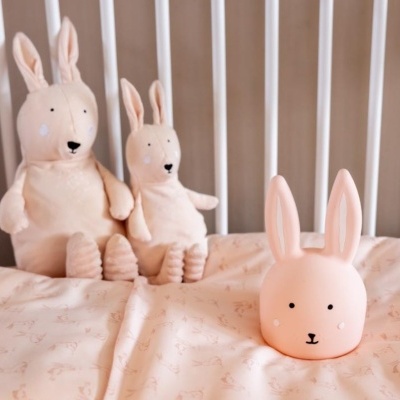 Três coelhos cor-de-rosa, dois peluches e um coelho rígido com orelhas grandes numa cama com colcha rosa