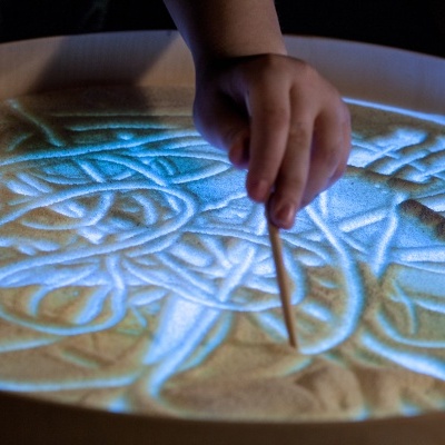 Mão de criança a desenhar numa mesa de areia iluminada a azul