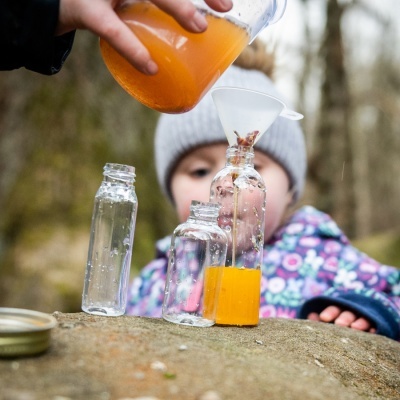 Três frascos de vidro com líquido laranja e criança ao fundo