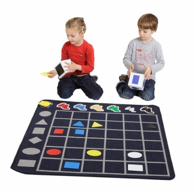 Duas crianças brincando num tapete educativo com formas coloridas e cubos grandes