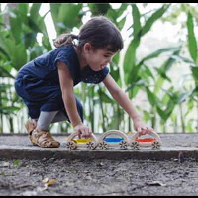Criança brincando ao ar livre com carros de madeira coloridos