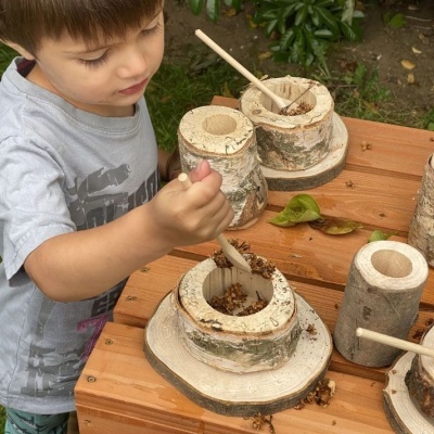 Criança a usar utensílios de madeira natural para mexer grãos em recipientes ao ar livre