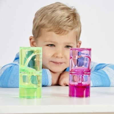 Dois copos medidores coloridos em plástico transparente numa mesa branca com menino ao fundo