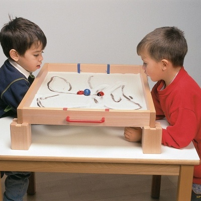 Duas crianças a jogar com tabuleiro de madeira sobre uma mesa branca em piso de madeira