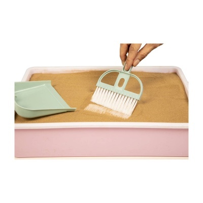 Pá e escova verdes claras com cerdas brancas numa caixa de areia cor-de-rosa