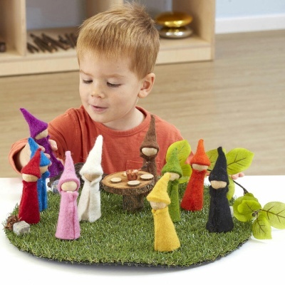 Criança brinca com gnomos coloridos de feltro sobre base verde de relva artificial.