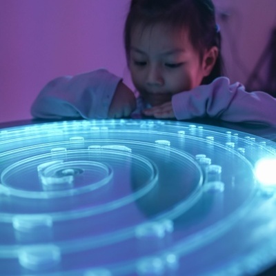 Criança a observar painel luminoso azul com padrão espiral.