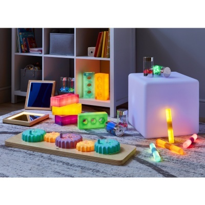 Brinquedos sensoriais coloridos em silicone com luzes sobre tapete cinzento perto de estante branca e cubo iluminado