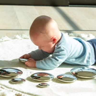 Bebé de bruços no tapete brincando com pedras metálicas