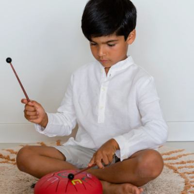 Criança a tocar instrumento vermelho sentado no chão sobre tapete