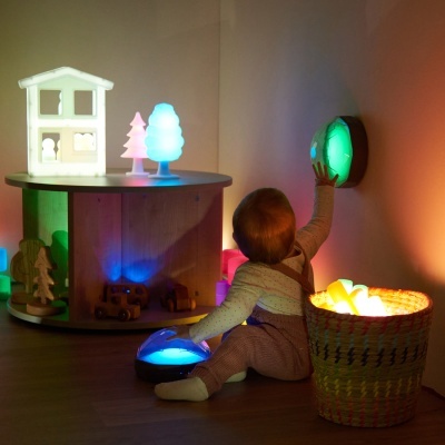 Brinquedos luminosos coloridos e bebé a brincar numa sala com paredes claras e chão em madeira.