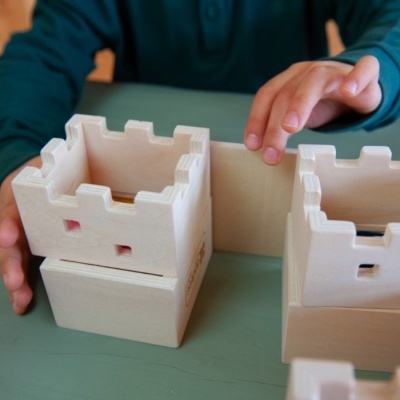 Brinquedo de madeira castelo empilhável em tom natural claro numa mesa verde com mãos a brincar